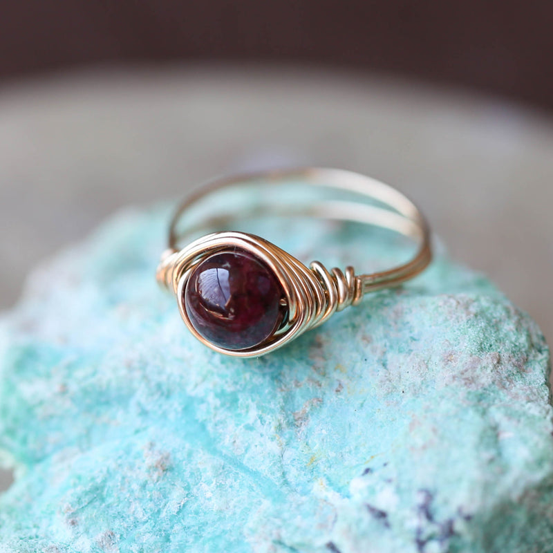 garnet gemstone ring displayed on rock with band and setting made of 14 gold filled